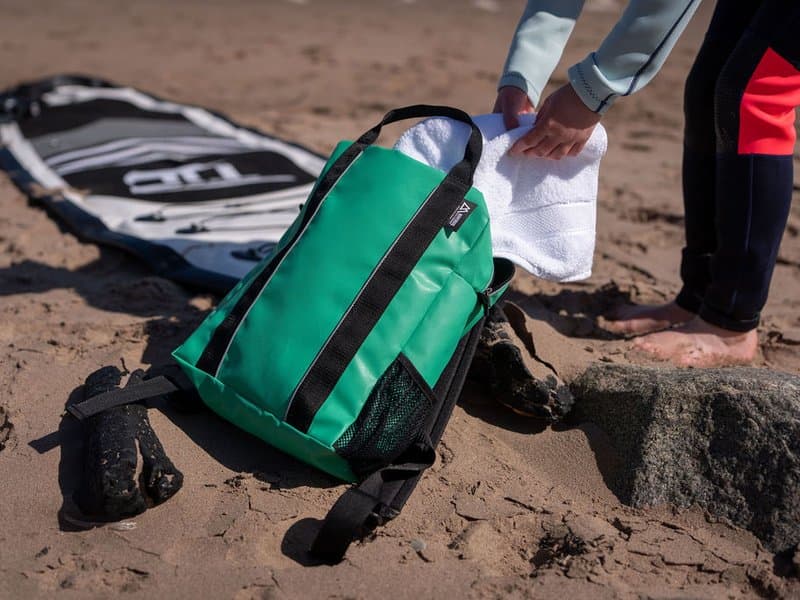 Montrose green backpack on the beach with surfboard
