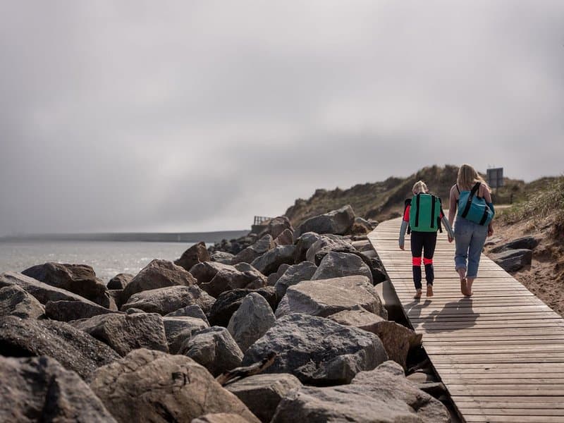 Swimmers walking along coastal boardwalk with Montrose bags