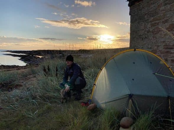 This image shows Dave with his dog Audrey next to a tent with a sunset in the background.
